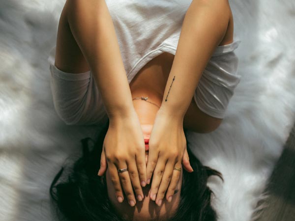 Woman in white lying on a fur carpet covering her face.