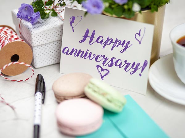 A card that reads “happy anniversary” sitting beside 3 french macaroons and a cup of coffee.