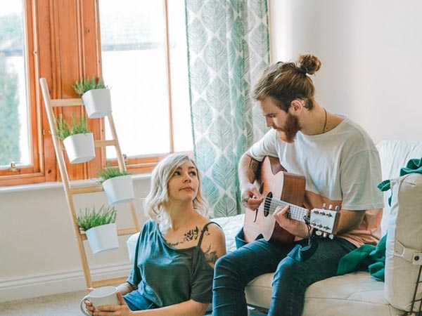 A man in a white shirt and jeans playing guitar to a girl.