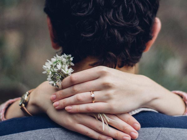 woman’s hand with ring and holding flowers wrapped around man’s neck