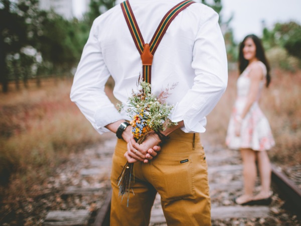 A photo of a man hiding fresh flowers at his back for his woman