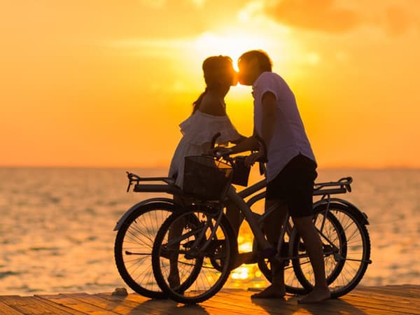 A couple kissing under the sunset while on a romantic bicycle date. 